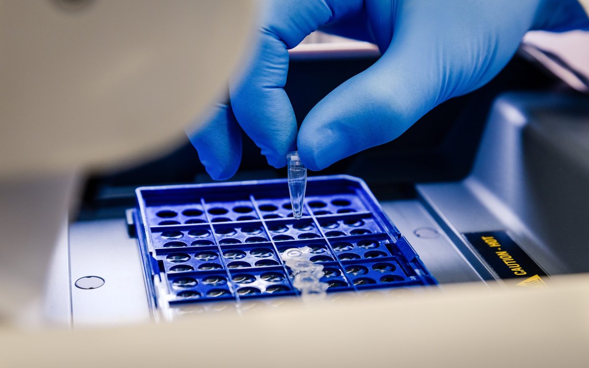 Loading a DNA sample tube into a PCR thermocycler in a molecular genetics laboratory